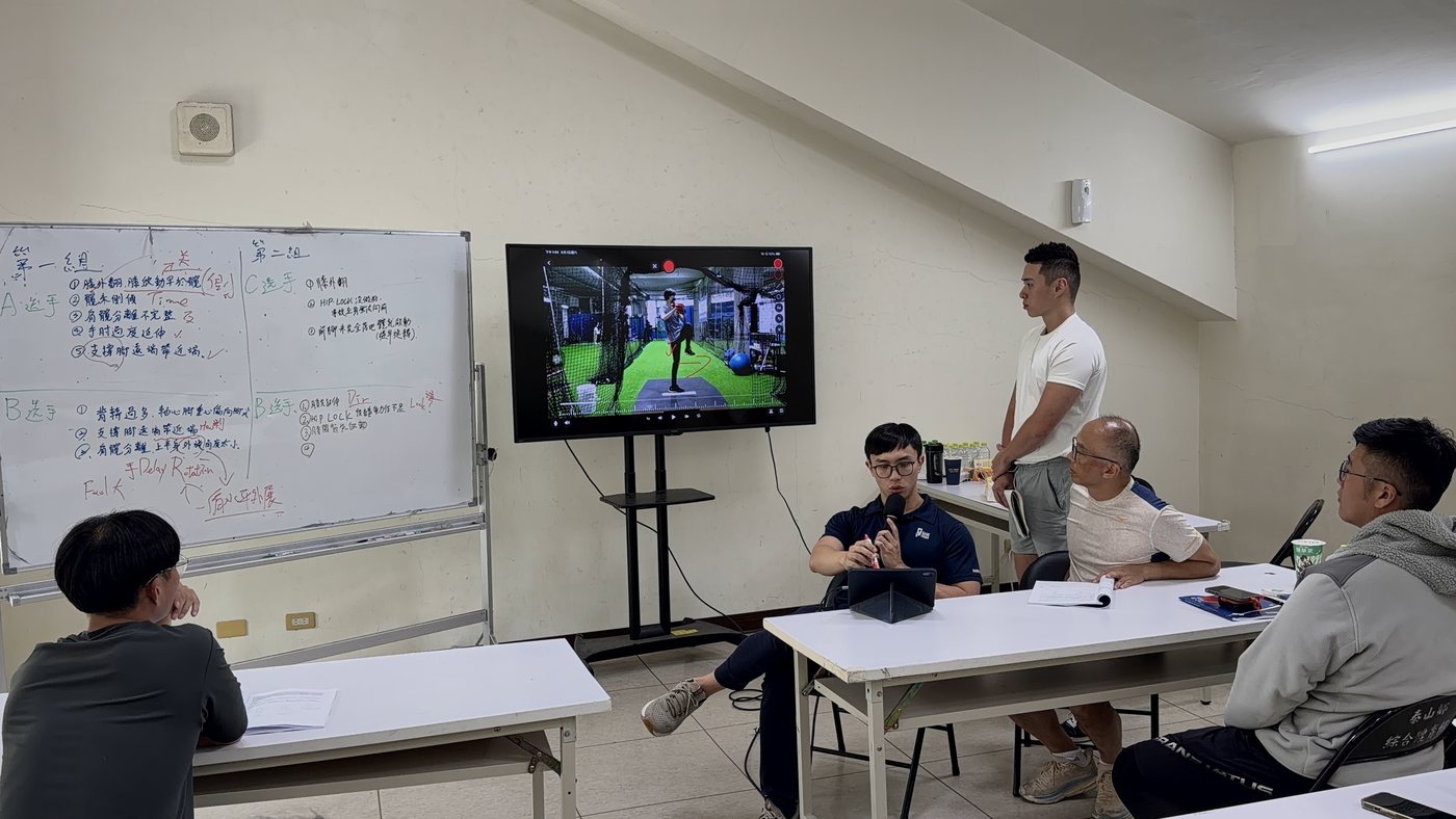 課堂上把投球影片投在螢幕上，旁邊白板寫著各組對選手的查核點分析